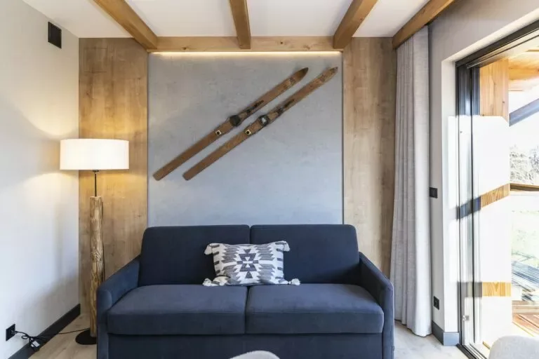 Apartament 0.3, Szymaszkowa 7 Zakopane – salon z sofą w odcieniu granatu i dekoracyjną ścianą z nartami w stylu retro