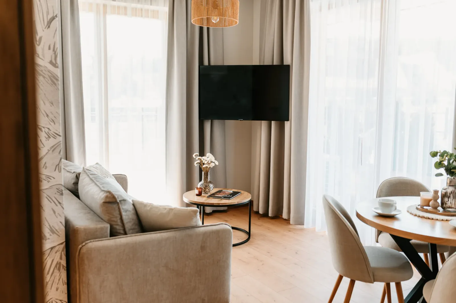 Jasny salon z sofą, stolikiem, telewizorem i częścią jadalnianą przy dużych oknach