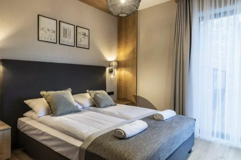 Szymaszkowa 7, apartament 0.9 - Sypialnia z grafitowym zagłówkiem, szarą narzutą i światłem wpadającym przez delikatną firanę