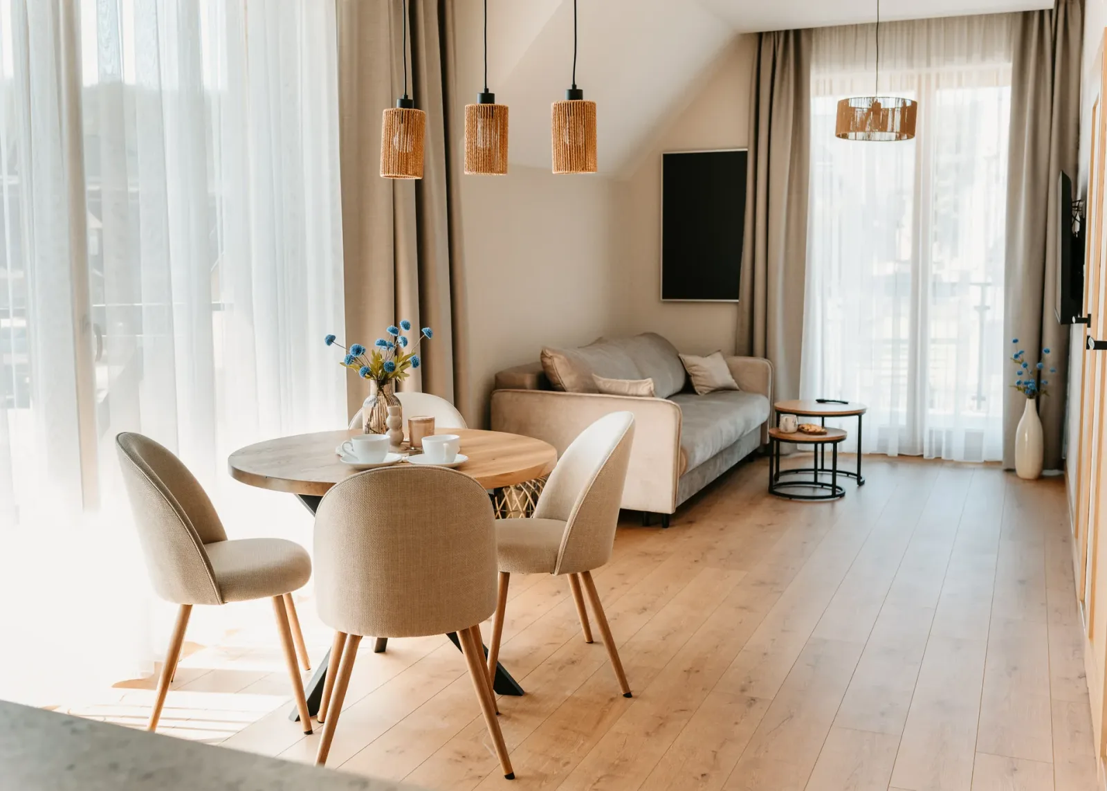Salon z jadalnią, okrągłym stołem i sofą przy dużych oknach