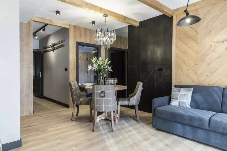 Salon Apartamentu 0.1, Szymaszkowa 7 Zakopane – ściany z jasnego drewna i ciemnego gresu, designerski żyrandol, okrągły stół i 4 krzesła