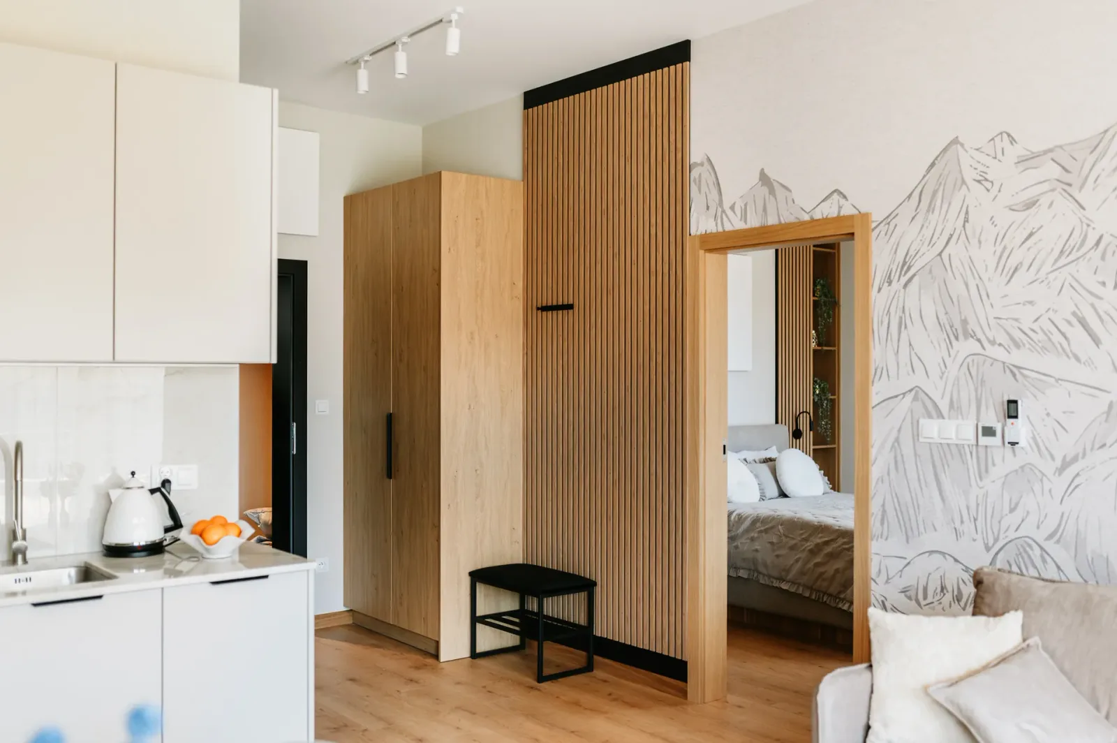 Aneks kuchenny, drewniana szafa i wejście do sypialni w jasnym apartamencie