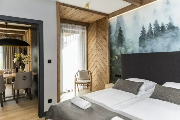 Sypialnia Apartamentu 0.2, Szymaszkowa 7 Zakopane – na pierwszym planie łóżko z grafitowym zagłówkiem, w tle część jadalna salonu i czarna designerska lampa